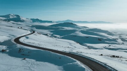 A winding road cuts through a snow-covered mountain landscape under a clear blue sky.