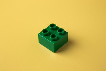 Green plastic building toy block on yellow background
