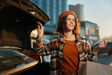 Woman shopping by car in an urban street at golden hour glow, smiling with paper bag beside open trunk, candid lifestyle moment of authenticity, mindful living and emotional storytelling.