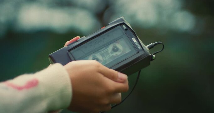 Close-up of a hand holding a vintage cassette player outdoors, evoking nostalgia and retro vibes. Symbolic moment mixing technology and emotion in nature.