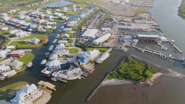 Slow-rotating drone view over the far end of Grand Isle, capturing waterfront homes, docks, decks, the event center, the marina, and Fifi River in a detailed coastal landscape.