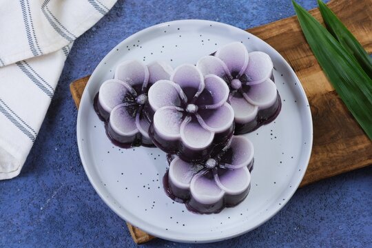 Beautiful steamed kue talam ubi ungu or purple Indonesian layered dessert shaped like flowers, arranged neatly on a white plate.