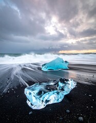 Clear blue glacial ice blocks on a black sand beach under a cloudy sky