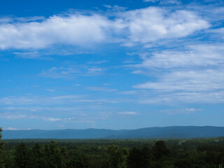 A scenic view of mountains and dense forest during the rainy season, covered in soft mist and rich greenery. The calm atmosphere and lush landscape create a peaceful and refreshing mood