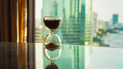 Hourglass on glass table with blurred modern cityscape background. Symbol of time, productivity, business pressure, and mindfulness. Ideal for concepts of time management and success in modern life.