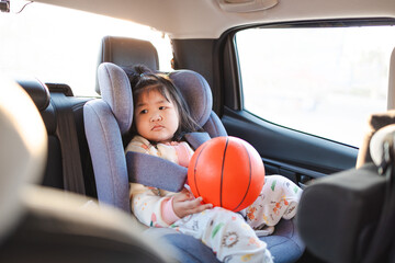 A cute little Asian girl sits hugging a basketball on the backseat of a car during a trip,Smiling...