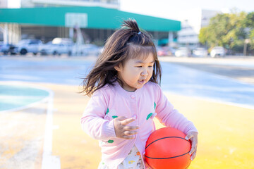 A cute little Asian girl is playing basketball on an outdoor court,A girl with basketball on court on summer season.