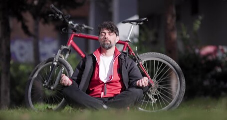 A peaceful scene of a man meditating outdoors with his red mountain bike parked beside him on a sunny day. - Powered by Adobe