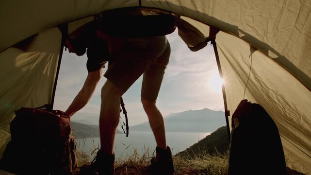 Traveler stepping out from tent picking backpack standing against sunrise concept of readiness motivation hope self discovery and new adventure in bright mountain morning
