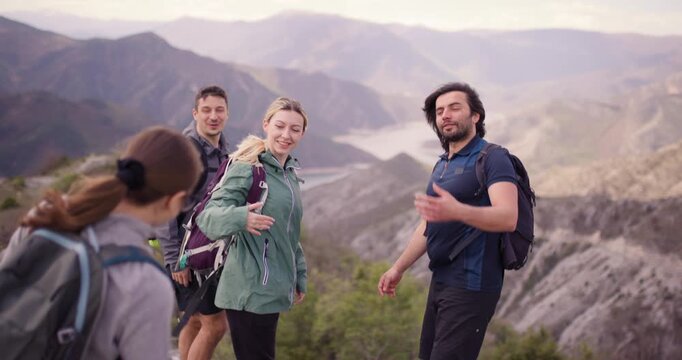 Group of friends with backpacks hiking in mountains, pausing to hug and enjoy the view, expressing joy and togetherness in nature.