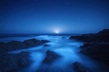 Tranquil rocky coastline under a starry night sky with soft glowing light on the horizon over calm ocean waves