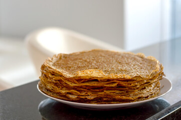 Thin lace pancakes on a plate in bright kitchen close up