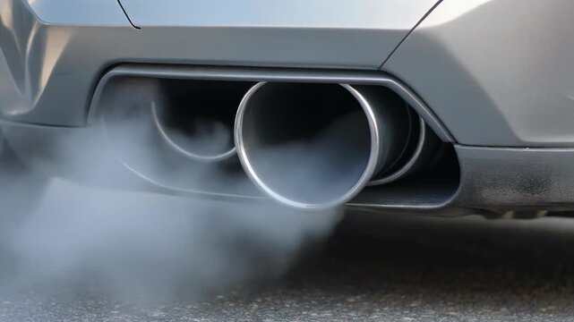 Close-up of a car's dual exhaust pipes emitting white smoke, indicating engine combustion or cold start.