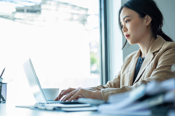 Businesswoman sitting at desk on couch in workplace or at home working on laptop and analyzing data on charts and graphs and writing on papers to make business plan and strategies for company.