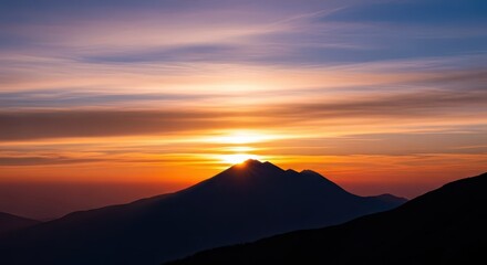 Brilliant sun emerges from behind a silhouetted mountain peak during twilight hours