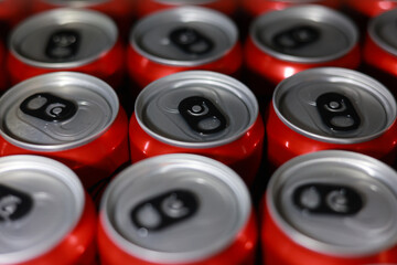 Close up top view background of many red aluminum cans of fizzy beverage. silver tops of soda cans create refreshing industrial pattern of refreshment
