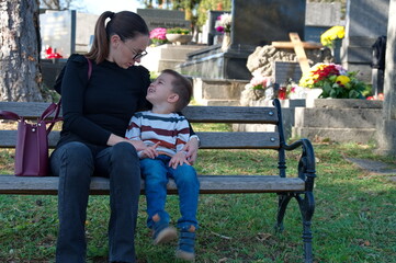 Mother and her little boy sitting on the bench in a cemetery
