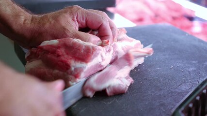 Hands of a professional butcher cutting a piece of raw bacon or pancetta with a knife.