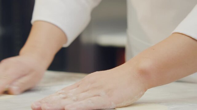 Chef's hands shaping and cutting the ravioli dough using artisanal techniques in a professional kitchen.