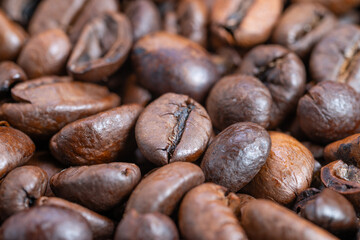 Richly roasted beans with oily sheen waiting to grind, Closeup of roasted coffee beans showcasing glossy oil layer and aromatic richness under bright studio illumination