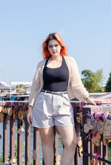 Asian beautiful woman vibrant hair smile wearing black top cozy cardigan light shorts, standing pose under warm sunlight calm waterside village create relaxed peaceful mood travel relaxation holidays.