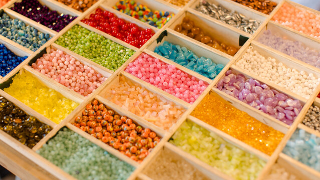 Vibrant collection multicolor craft beads neatly arrange in wooden organizer boxes compartment showcases unique textures hues, handcrafted creating charming slow fashion bracelets inspiring display.