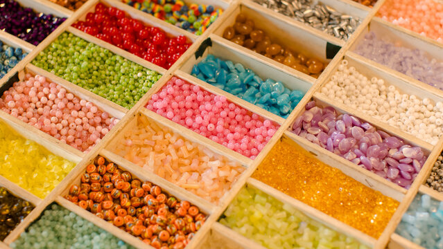 Vibrant collection multicolor craft beads neatly arrange in wooden organizer boxes compartment showcases unique textures hues, handcrafted creating charming slow fashion bracelets inspiring display.