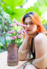 Asian happy beautiful cheerful outdoor portrait woman light orange hair smiling warmly among blooming bouquet flowers, Natural tree cafe greenery create cozy rustic garden joyful fresh nature concept