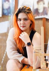 Asian happy beautiful cheerful portrait young woman light orange long hair smiling sitting art themed coffee shop cafe, natural wooden textures create joyful relaxation travel holidays lifestyle.