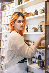 Asian happy beautiful cheerful portrait young woman light orange long hair smiling standing select to view handicrafts pottery shop on white wooden shelves joyful relaxation travel holidays lifestyle.