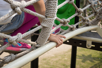 A close up of a child climbing a rope net at a playground, highlighting textures of the ropes and clothing.