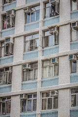 Fototapeta premium A residential building facade with metal barred windows, blue tile bands, and air conditioning units in an urban setting.