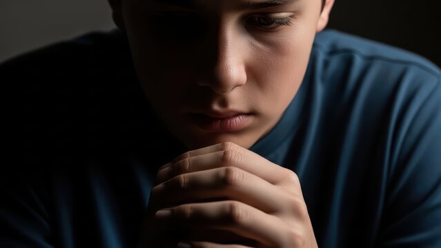 Young male teen contemplating in low light with thoughtful expression