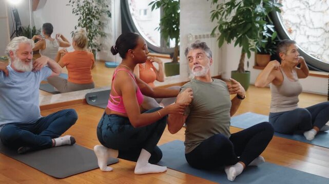 Black female fitness instructor guiding an older man through proper arm stretching during a senior group class. A group of seniors at a joint fitness class with a female trainer.