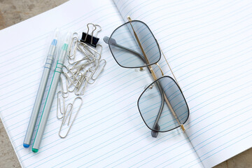 Stationery items on a lined notebook with eyeglasses, representing studying, office work, and a simple organized workspace, Top view