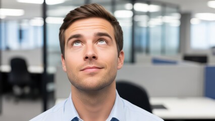 Young male in office looking upward with thoughtful expression
