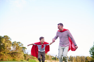 Park, child and dad with superhero costumes, family and fun with imagination, bonding and happiness. Outdoor, man and son with cape, pretend and holding hands with boy in nature, mockup space or play