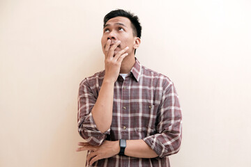 Southeast Asian man wearing flannel shirt  thinking about something while looking to upper right corner, on white isolated background