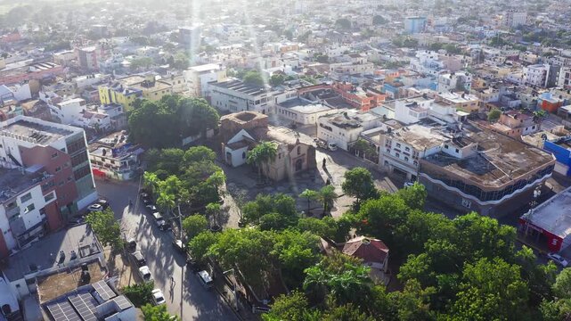 Aerial drone view of the historic San Dionisio Church in Hig&uuml;ey. The colonial-style sanctuary stands in a green plaza surrounded by the urban cityscape of the Dominican Republic.