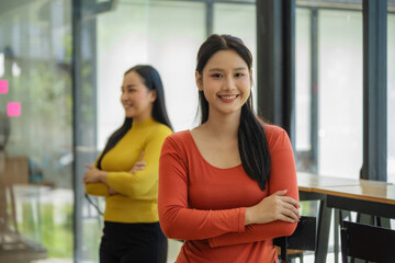 Portrait of a young beautiful female office worker keeping arms crossed, looking at camera and...
