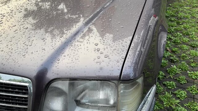 Close-up rain droplets on vintage car hood and headlight, water droplets on metallic surface during light rain, detailed automotive texture shot