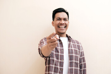 Southeast Asian man wearing flannel shirt cheerful expression while  pointing at the camera with...
