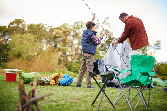 Father, boy and building tent for camping, outdoor and back with help, guide or teaching in nature. People, dad and son at campsite, shelter or support for learning survival skills on family vacation