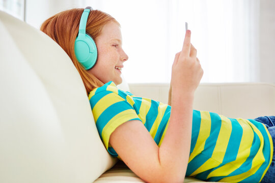 Happy girl, relax and playing with headphones or tablet on sofa for games, music or podcast in home. Kid, child or teenager with technology or sound app for audio streaming or entertainment in house - Powered by Adobe