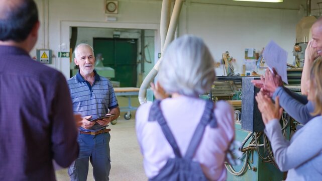 Senior craftsman receiving applause from workshop team - Powered by Adobe
