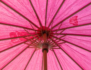 Close-up of the underside of a vibrant, pink, paper umbrella. The wooden ribs and central pole are visible, creating a radial pattern