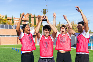 Happy multi ethnic soccer team raising a trophy, celebrating winning a football tournament on a sunny outdoor sports field