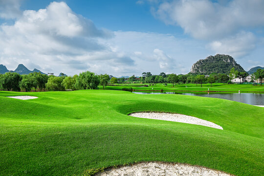 Green golf course field with sand bunkers and lake in summer.