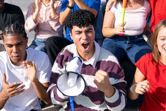 Multiethnic young adult fans shouting, clapping, and laughing while supporting team at sport event in a stadium