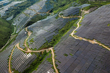 Aerial view of large solar farm panels on mountain slopes with winding road.